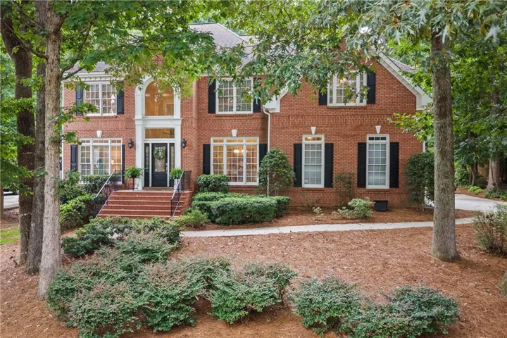 Traditional brick exterior featuring a grand arched entryway, multiple double-hung windows with black shutters, and an inviting front porch with wrought iron railings
