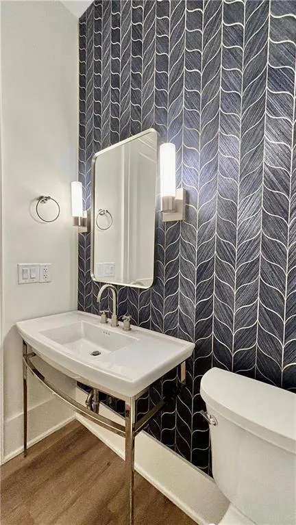 Half bathroom featuring wallpapered walls and wood finished floors