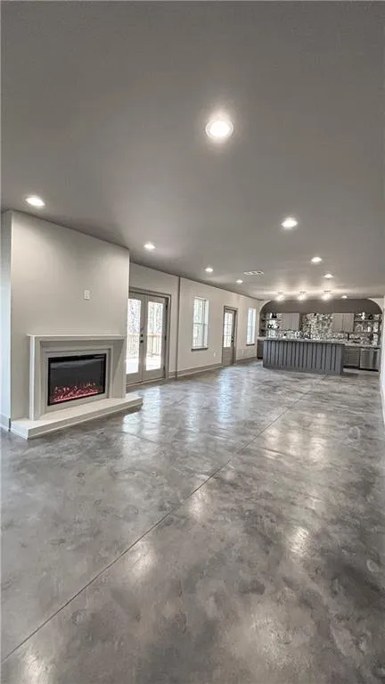 Unfurnished living room with finished concrete floors, plenty of natural light, a warm lit fireplace, recessed lighting, and french doors