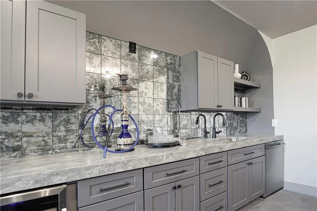Bar area featuring gray cabinetry, open shelves, dishwasher, backsplash, and beverage cooler