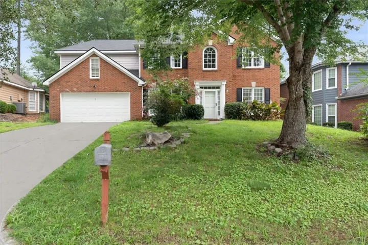 Traditional brick and siding exterior featuring an attached two-car garage, white paneled entry door, and multiple windows with dark shutters
