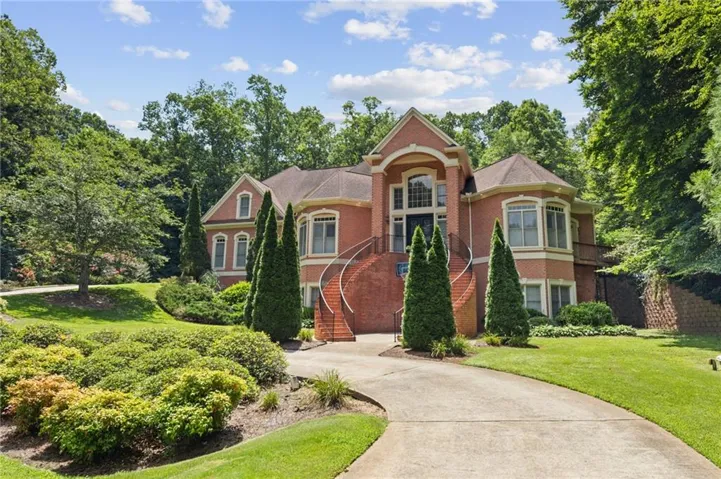 Brick facade residence featuring a grand entrance with curved staircases, a prominent bay window, a multi-pane arched window, and a concrete driveway