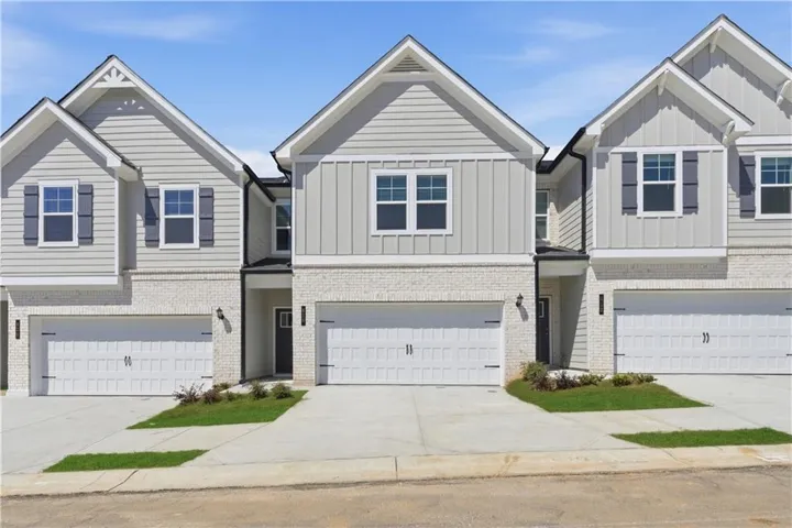 Modern townhome exterior featuring light-colored siding, white brick accents, dark decorative shutters, and individual two-car garages with carriage-style doors