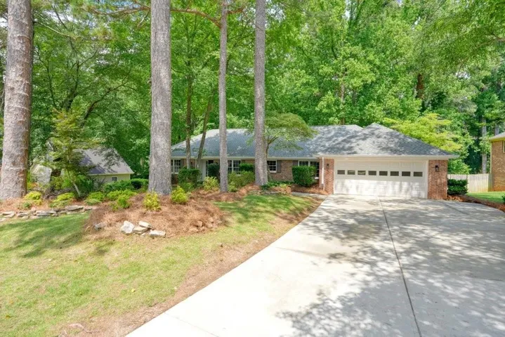 Brick exterior home featuring a two-car garage, mature trees, and a concrete driveway