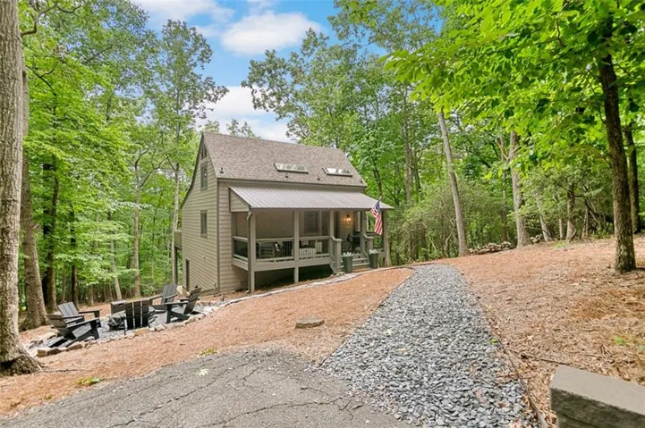 Wooded property featuring a screened porch, a pitched roofline, and a gravel pathway