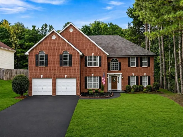 Brick exterior with white garage doors, asphalt driveway, and a manicured lawn