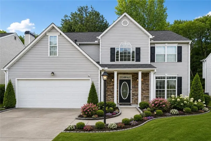 Siding exterior with stone accents, a covered entry, an arched window, a two-car garage, and a landscaped front yard