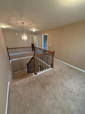 Upper-level landing featuring neutral carpet, a wood banister with black metal spindles, and a central chandelier