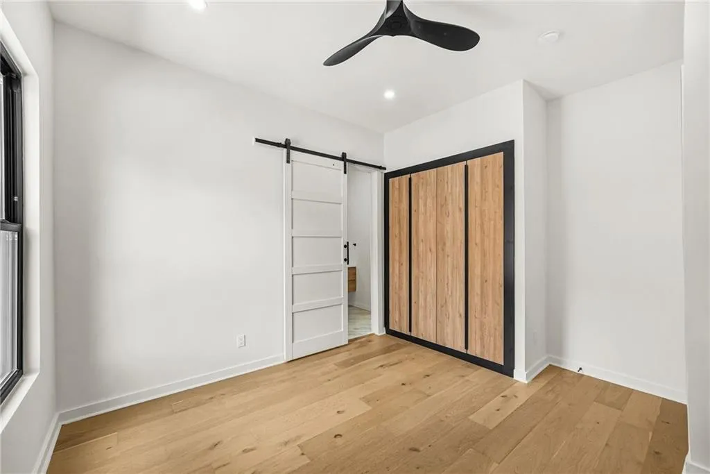 Warm wood-finish flooring with a modern ceiling fan, recessed lighting, and a white barn door