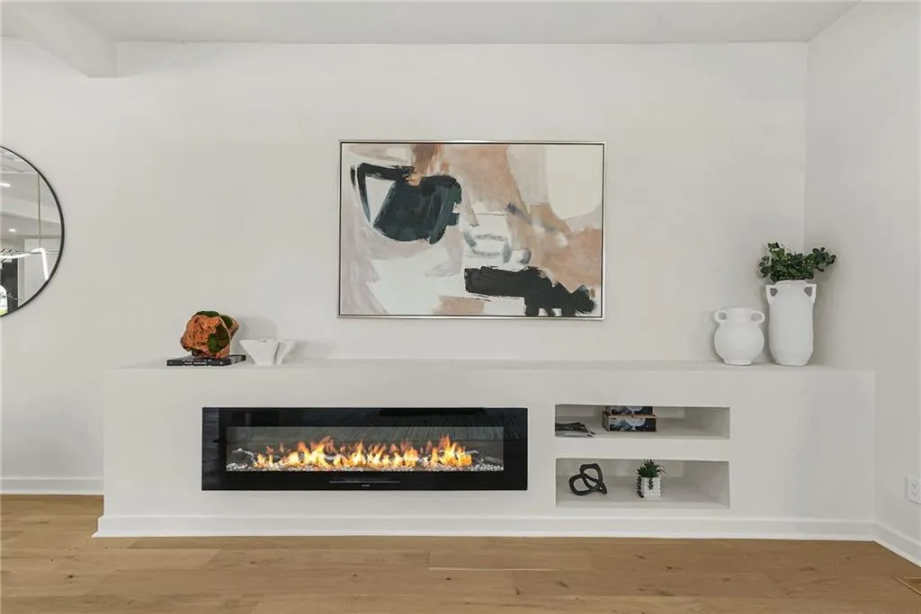 Built-in linear fireplace with a solid surface hearth, integrated shelving, wood-finish flooring, and crisp white walls
