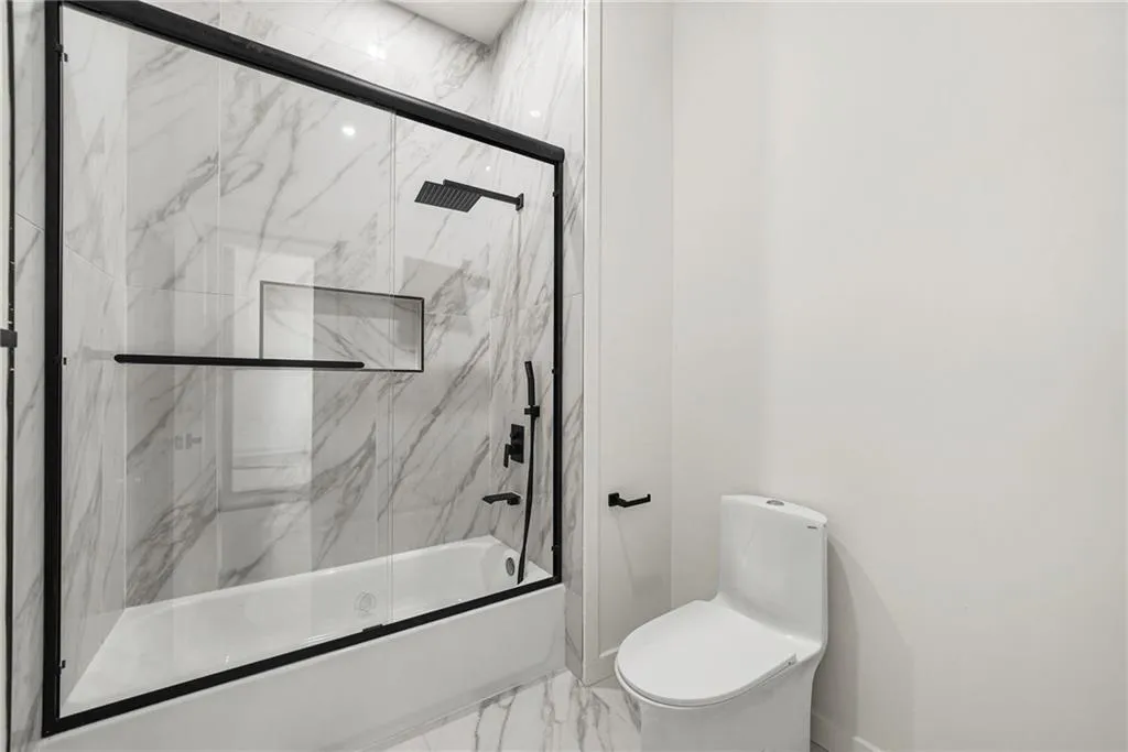 Bathtub with a glass enclosure, a matte black showerhead, and wall-mounted controls