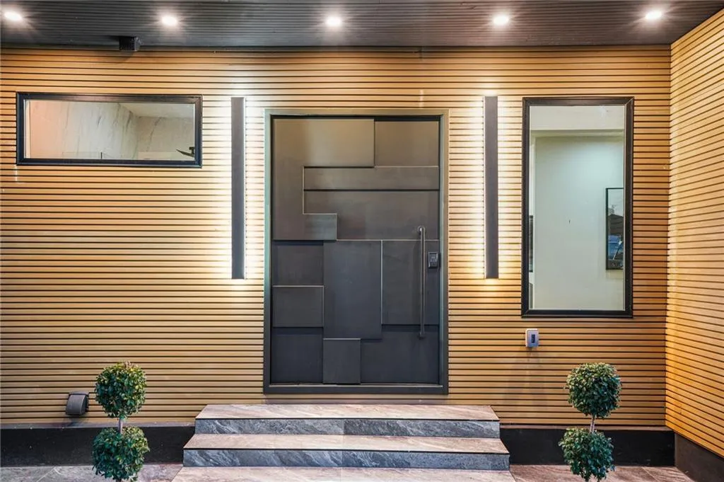 Wood-paneled exterior with a geometric-patterned entry door, integrated vertical lighting, and recessed ceiling lights