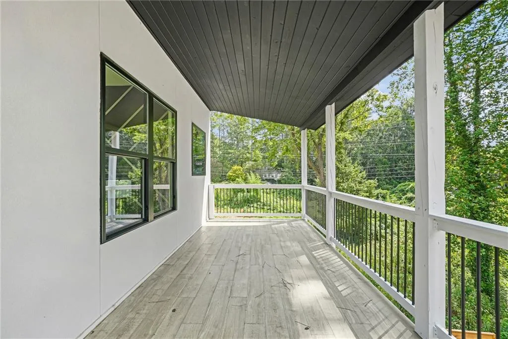Covered outdoor deck with wood-finish flooring, white railing, and black balusters