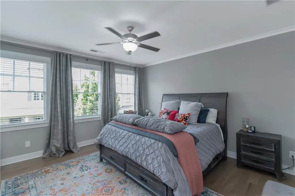 Bedroom with a ceiling fan, baseboards, wood finished floors, visible vents, and ornamental molding