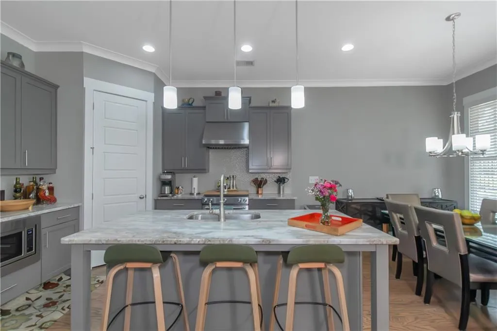 Kitchen with a sink, gray cabinets, under cabinet range hood, and crown molding
