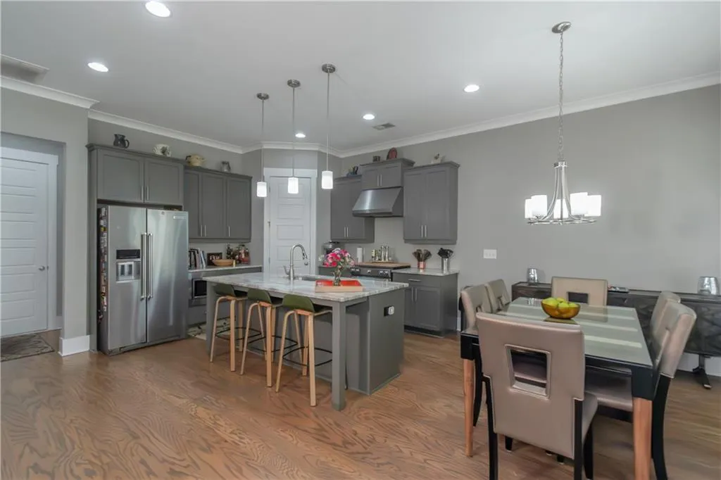 Kitchen featuring gray cabinets, a notable chandelier, a breakfast bar, under cabinet range hood, and high end fridge