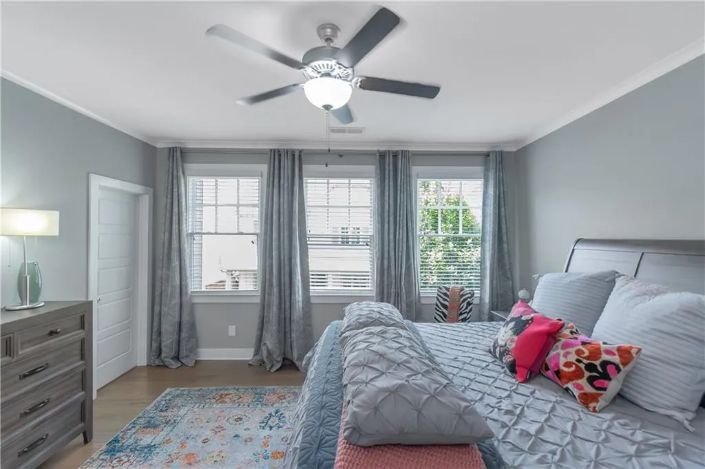 Bedroom with ceiling fan, baseboards, wood finished floors, visible vents, and ornamental molding
