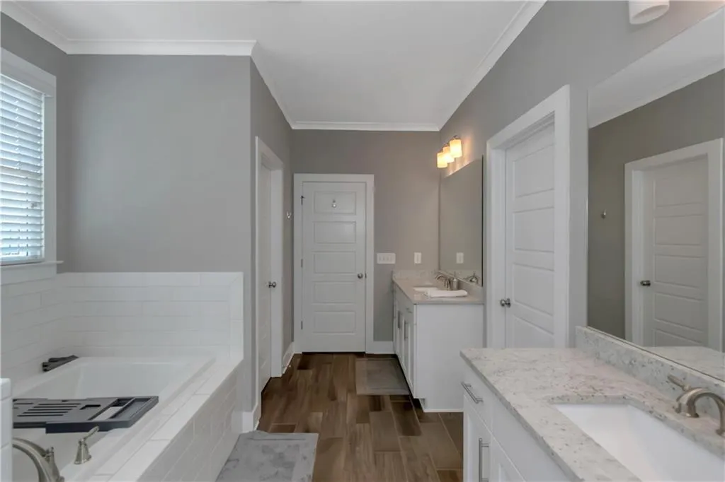 Bathroom with a bath, wood finished floors, two vanities, a sink, and ornamental molding