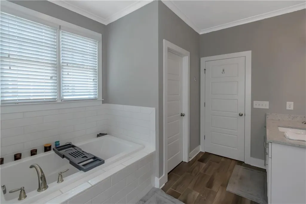 Full bath featuring a garden tub, wood finished floors, vanity, baseboards, and ornamental molding