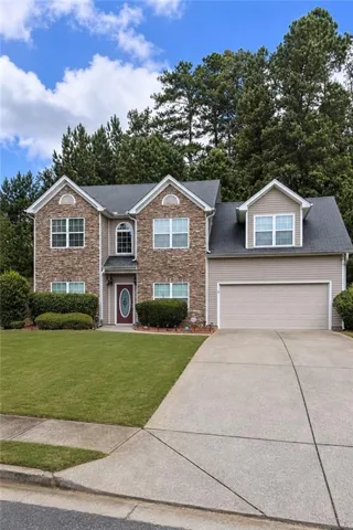 Two-story exterior with a stone and siding facade, featuring a red entry door, an attached garage, and a concrete driveway