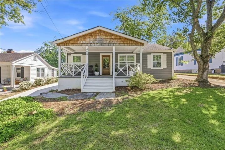 Charming cottage exterior featuring a covered front porch with white railings, natural wood shingle accents, dark siding, and white window shutters