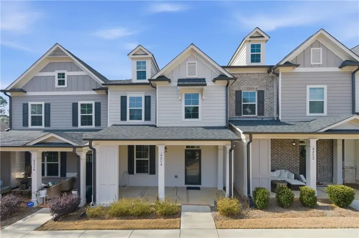 Contemporary townhome exterior featuring light-colored siding with dark window shutters, a covered front porch, and a dormer window
