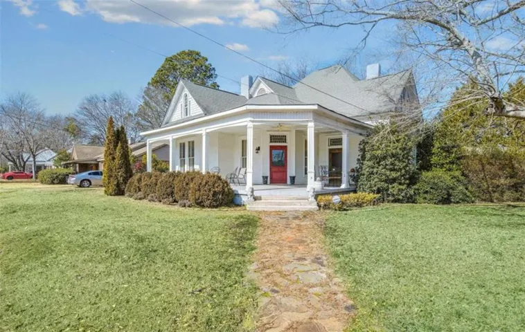 Victorian-style residence featuring a prominent covered front porch with white columns, a vibrant red entry door, and a stone pathway
