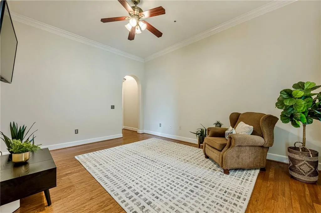 Living area featuring arched walkways, ornamental molding, light wood-type flooring, and a ceiling fan