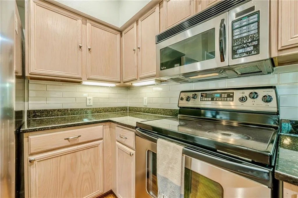 Kitchen with light brown cabinets, appliances with stainless steel finishes, tasteful backsplash, and dark stone countertops