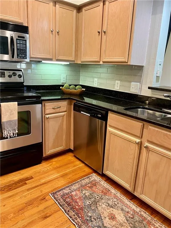 Kitchen featuring appliances with stainless steel finishes, tasteful backsplash, light brown cabinetry, and dark stone counters