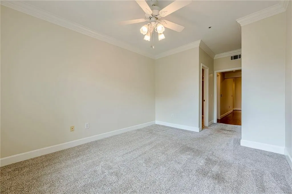 Second bedroom with light carpet, ornamental molding, and a ceiling fan