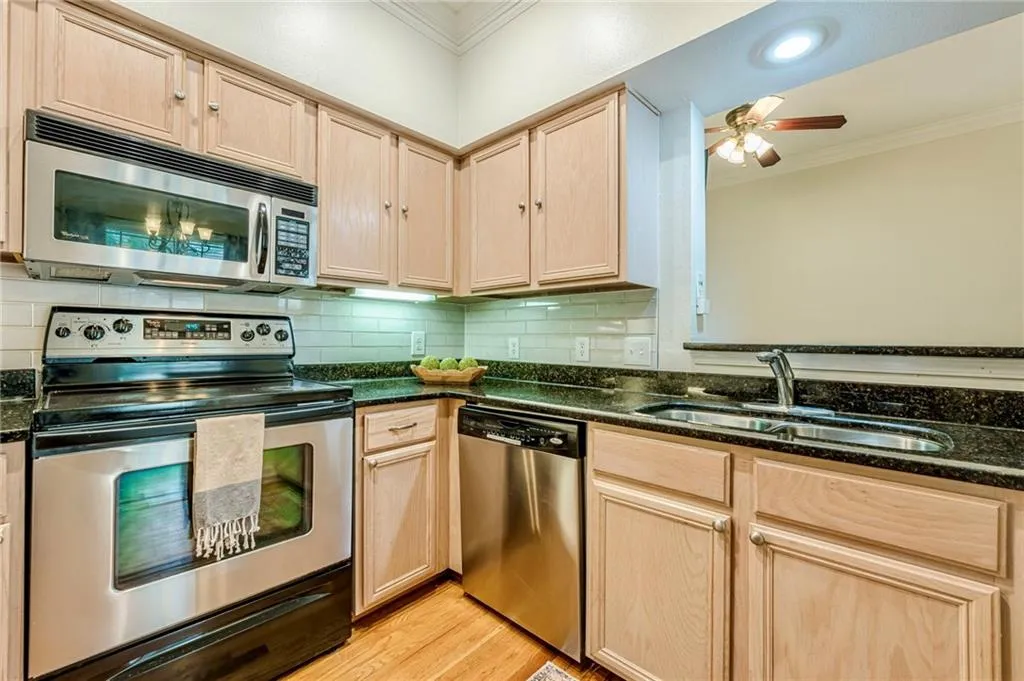 Kitchen featuring ornamental molding, light brown cabinets, appliances with stainless steel finishes, light wood-type flooring, and dark stone counters