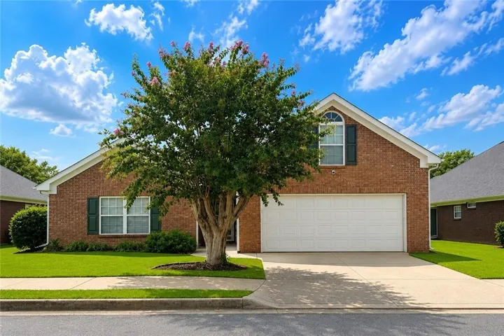Brick exterior with an attached two-car garage, concrete driveway, and front lawn