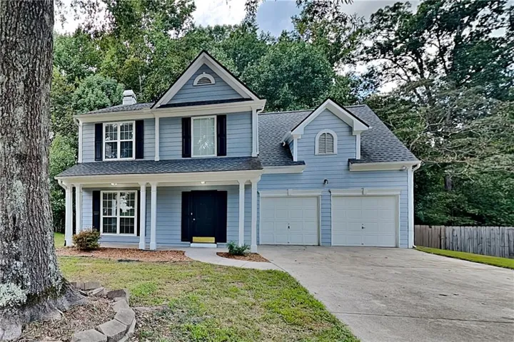 Light blue exterior with white trim, covered front porch, prominent dormer windows, and attached two-car garage