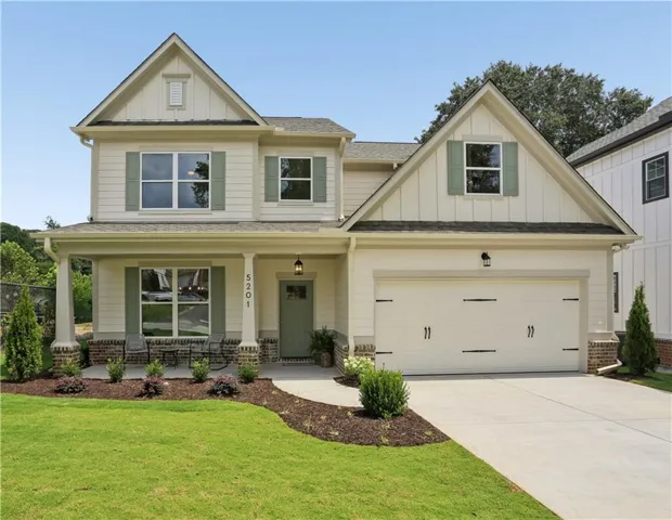 Two-story residence featuring a covered front porch with column supports, board and batten siding accents, a two-car garage with decorative hardware, a concrete driveway, and mature landscaping