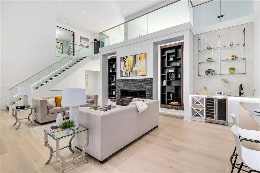 Living room with built in features, a towering ceiling, beverage cooler, a glass covered fireplace, and stairs