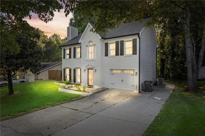 Two-story residential exterior featuring a white brick and siding facade, black window shutters, a front-entry garage, and a concrete driveway