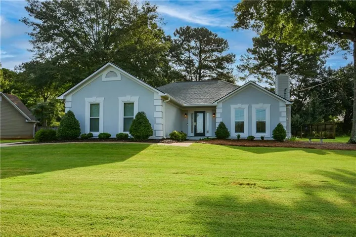 Light blue exterior with white trim details, featuring a prominent front lawn, mature trees