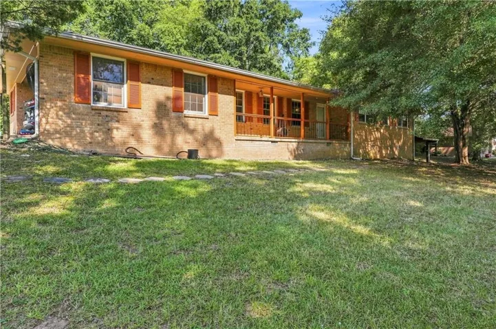 Brick exterior with a covered front porch featuring wood railing, multiple windows with shutters, and a sloped front lawn