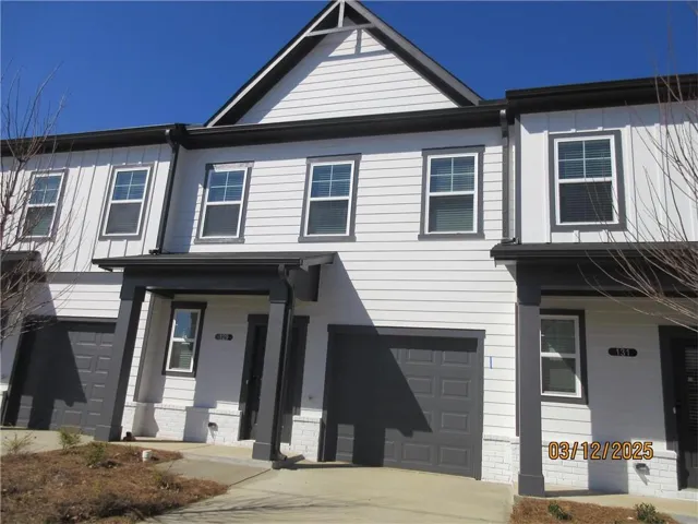 Modern townhome exterior featuring white siding, dark trim accents, multiple windows, and an attached garage