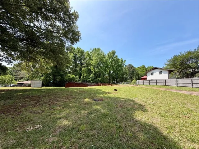 Expansive grassy lot with mature trees, a partial privacy fence, and a clear sky backdrop