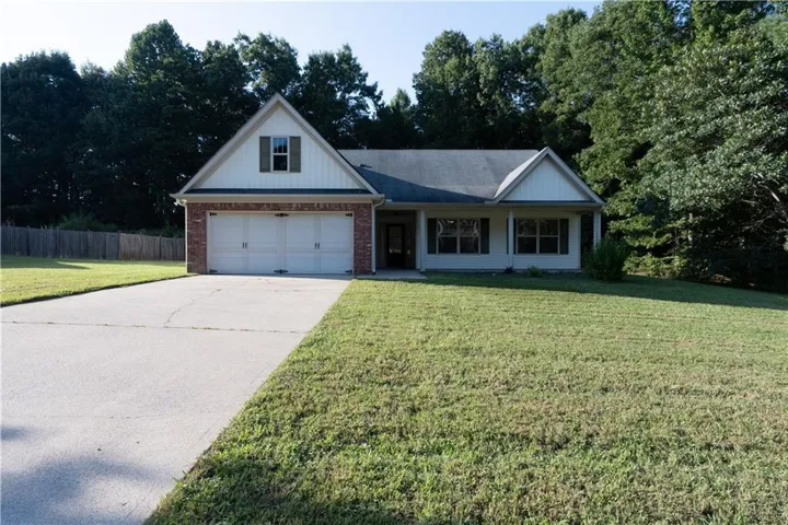 Brick and siding exterior with a two-car garage, mature trees, and a concrete driveway