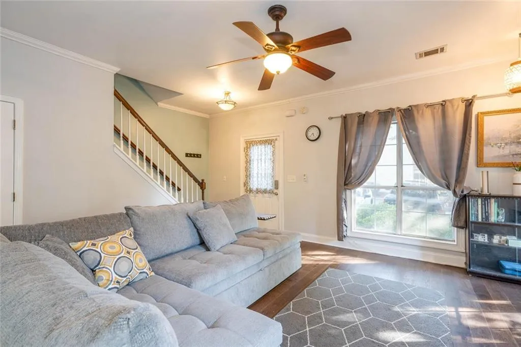 Living room with ceiling fan, dark wood-type flooring, and crown molding
