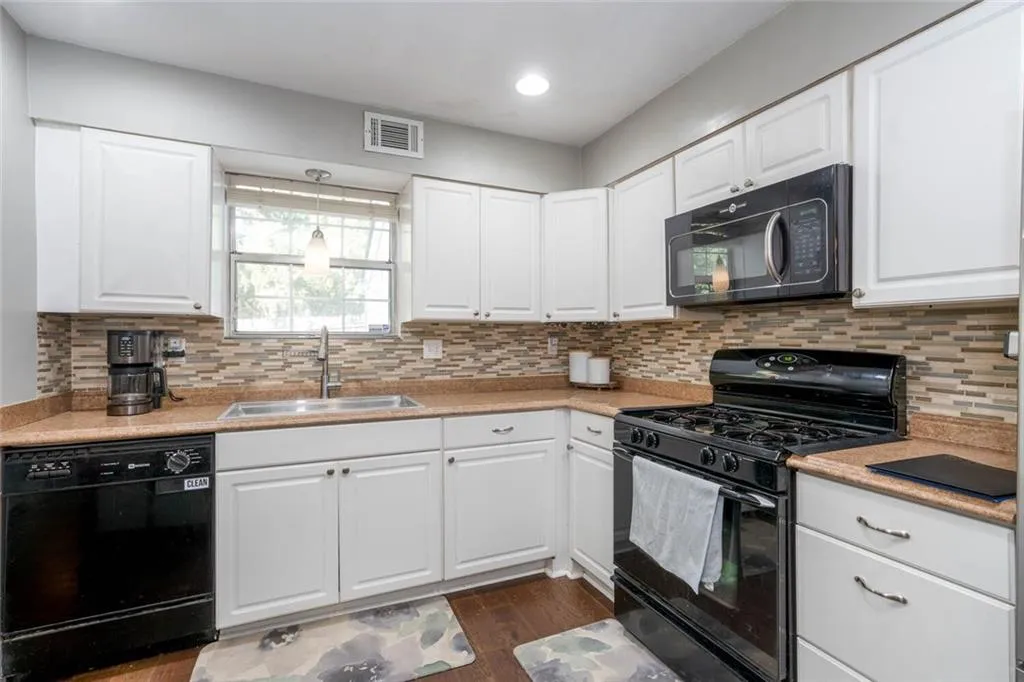 Kitchen with white cabinets, black appliances, sink, and dark hardwood / wood-style flooring