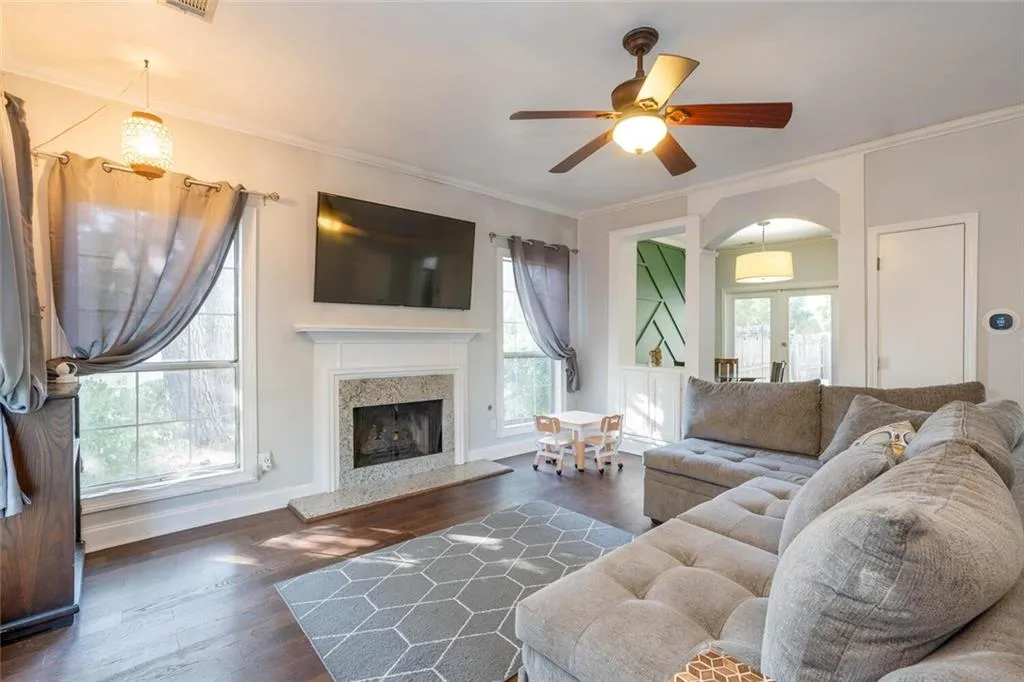 Living room with dark wood-type flooring, a high end fireplace, crown molding, ceiling fan, and french doors