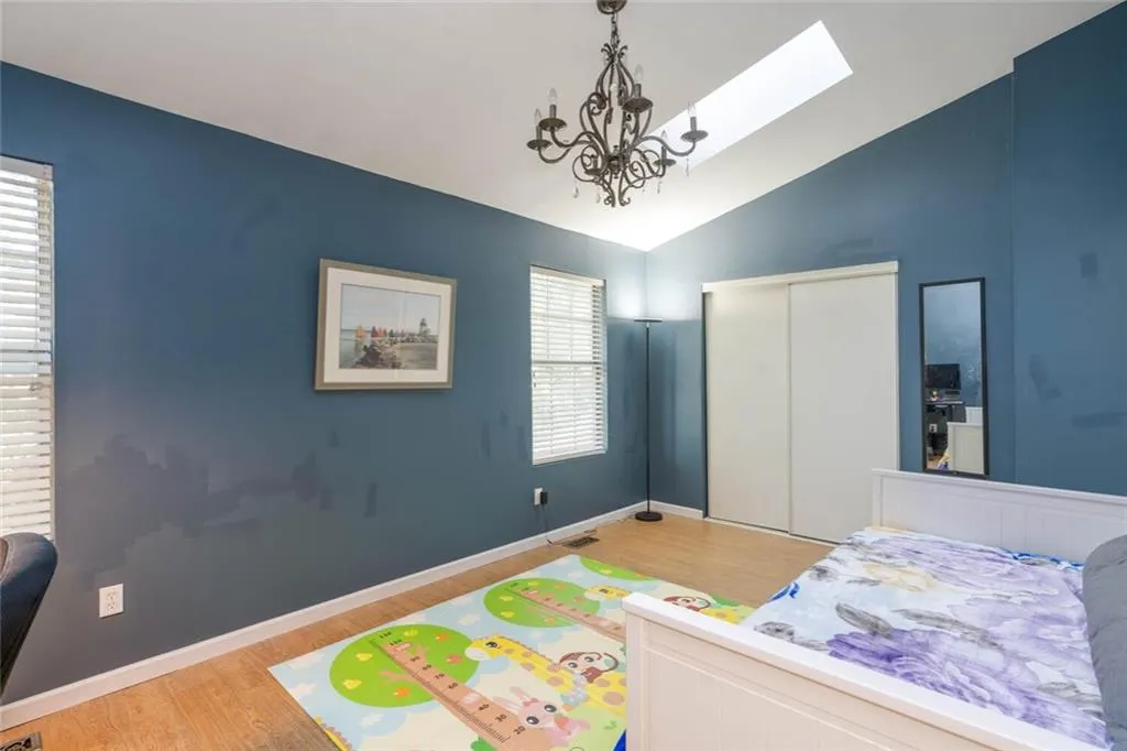 Bedroom with a notable chandelier, light wood-type flooring, vaulted ceiling, and a closet