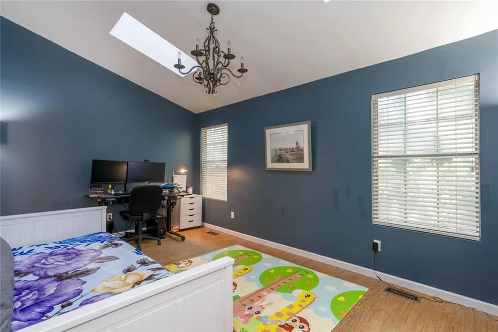 Bedroom with vaulted ceiling with skylight, light hardwood / wood-style flooring, and a chandelier