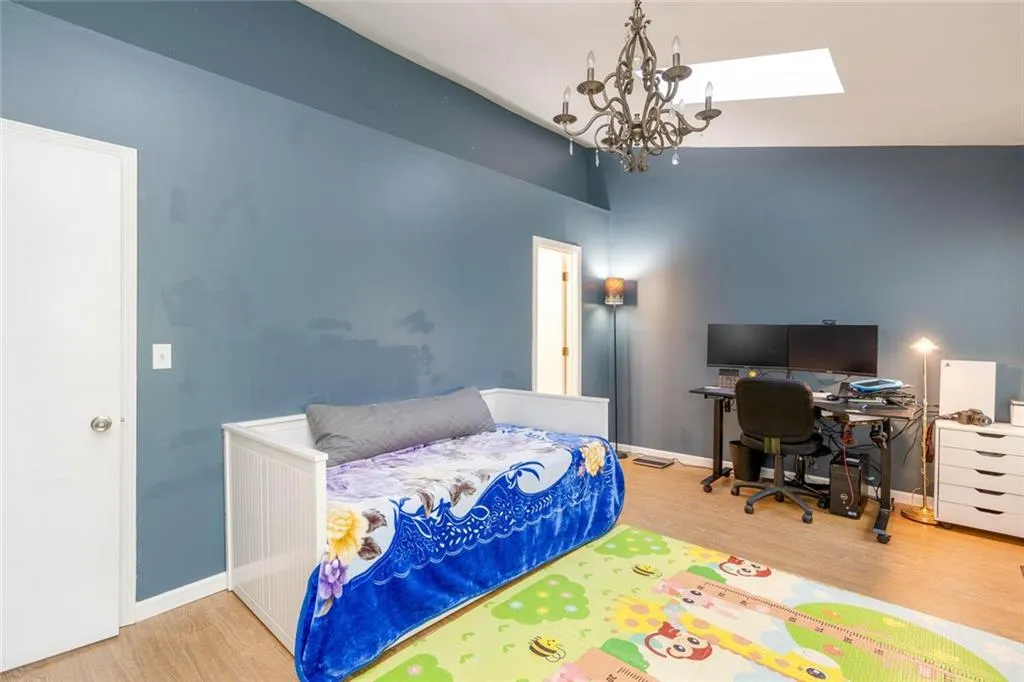 Bedroom with wood-type flooring, a notable chandelier, and lofted ceiling