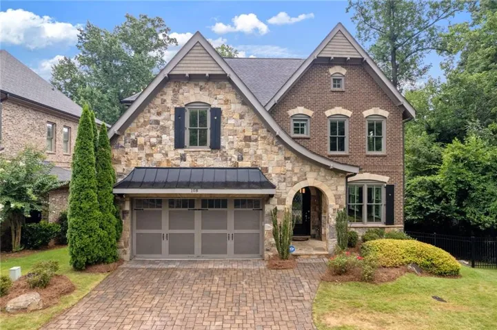 Elegant two-story brick and stone Colonial featuring a covered entry portico, multi-pane windows with black shutters, and a metal roof accent