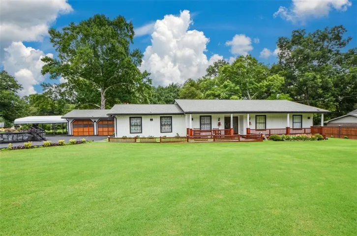 Front exterior featuring a wide lawn, a covered porch, white siding, and a two-car garage with wood-finish doors